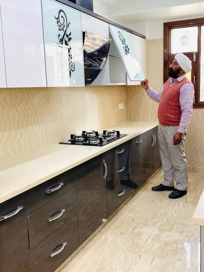 Here, one of our senior craftsmen inspects a newly installed kitchen. It features a two-tone design with glossy grey base cabinets and white upper cabinets with a decorative glass pattern.