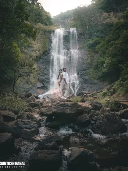 A stunning, moody shot of a couple posing on rocks in front of a large waterfall.