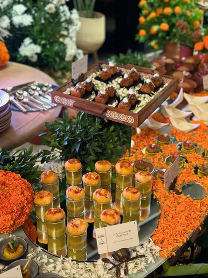 A wide shot of a festive appetizer station, featuring multiple tiers of different canapés. The vibrant colors of the food and the marigold decorations create a visually stunning and abundant display.