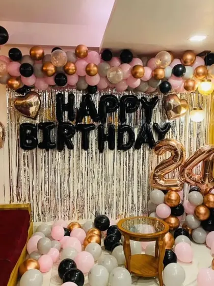 A 24th birthday party at home with a silver shimmer curtain, 'HAPPY BIRTHDAY' foil balloons, and a garland in pink, black, and grey.