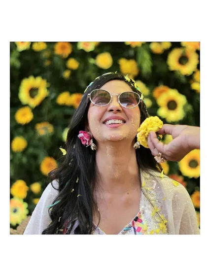 A beautiful close-up of the bride during her Haldi. A friend gently applies flower petals to her face, a sweet and gentle moment amidst the vibrant celebration.