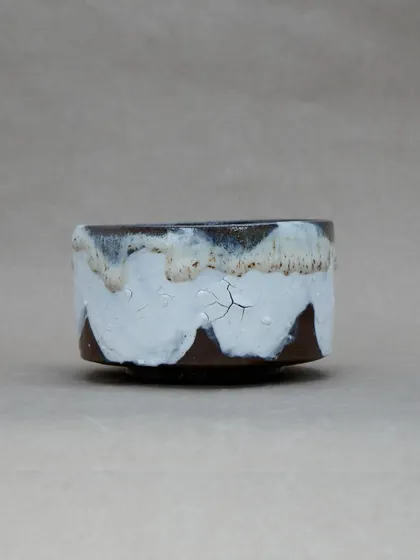 A simple tea bowl with a dramatic, dripping glaze. The thick white glaze cracks and pulls over the dark clay body, creating a landscape of texture.