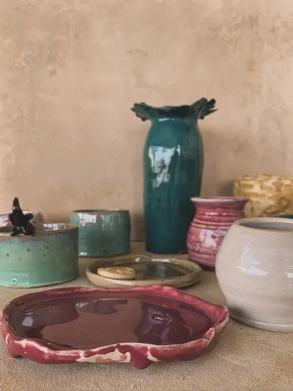 A collection of glazed pieces, including a magenta plate, a small vase, and a textured pot. The different colors and forms create a beautiful, eclectic group.