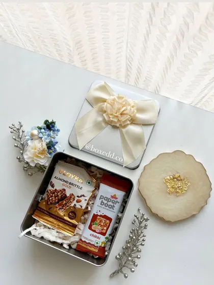 A thoughtful and useful return gift set. This tin box contains gourmet almond brittle and chikki, paired with a beautiful resin coaster, offering a mix of taste and home decor.