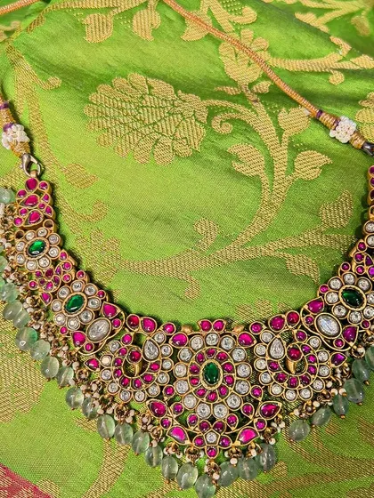 A beautiful Jadua Kundan choker with red and green stones and light green bead drops. This piece sits beautifully on the neck and is perfect for a festive look.