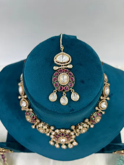 A pair of Moissanite Kundan earrings with a circular design. The ruby-colored stones and white stone drops make these a vibrant and attractive choice.