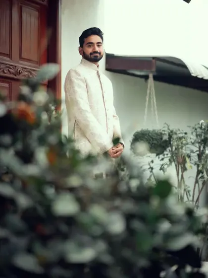 A candid shot of the groom, framed by greenery, as he waits for the ceremony to begin.