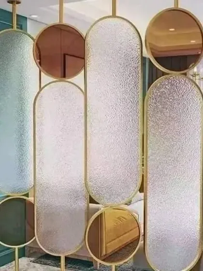 This artistic partition combines frosted and colored glass panels of different shapes within a gold frame, acting as both a room divider and a piece of modern art.