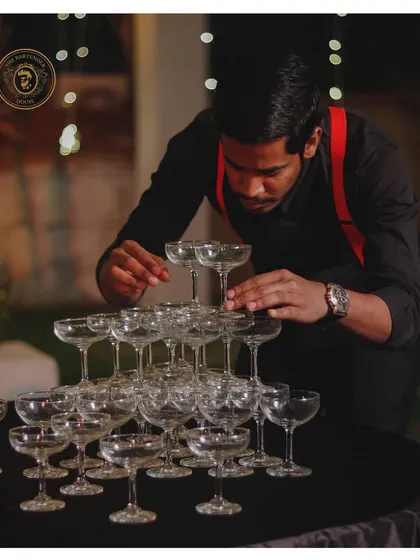 The foundation of a celebration. A team member carefully constructs a champagne tower, a classic symbol of luxury and joy at any wedding or grand event.
