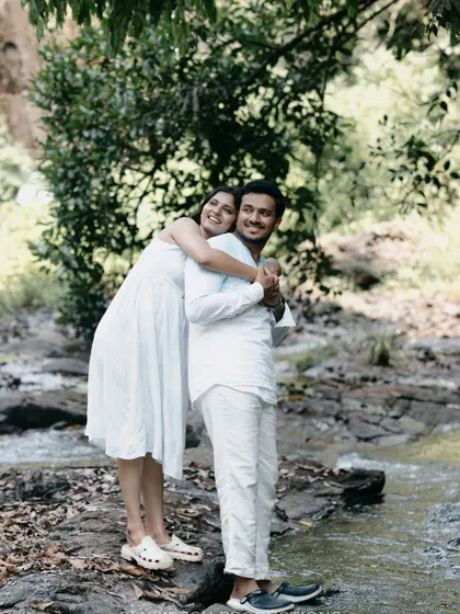 A happy, full-length shot of a couple by a stream in Coorg, dressed in white, blending perfectly with the natural scenery.