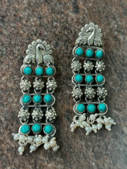 Pure silver earrings featuring a peacock motif and vibrant turquoise stones. The design is finished with delicate pearl drops, adding a touch of elegance and movement.