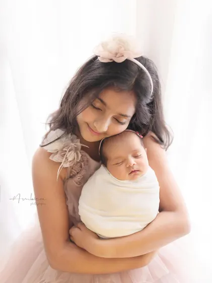 A close-up of the sweet, protective bond between sisters. The older sister's gentle smile as she holds the sleeping newborn is a moment of pure tenderness.