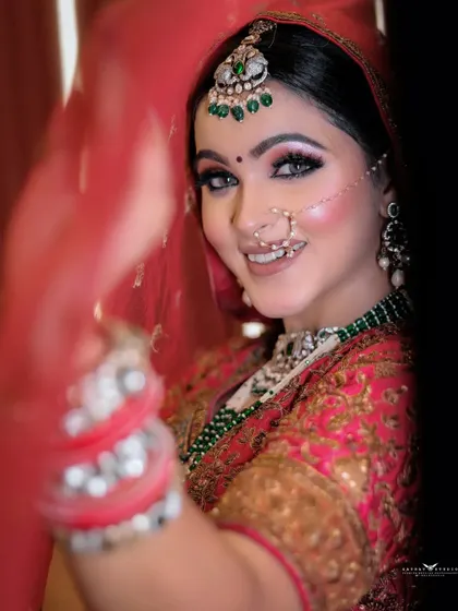 A happy bride peeks through her veil with a bright smile. This photo is full of joy and playfulness, capturing a classic moment in Indian bridal photography.