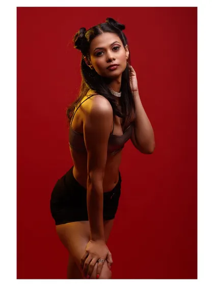 A high-energy studio shot with a bold red background. The metallic top and playful hairstyle create a fun and modern vibe.