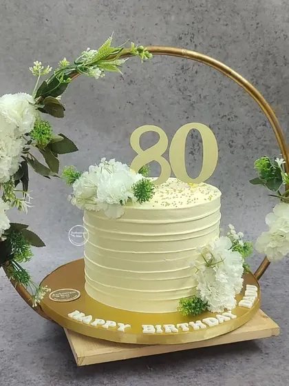 A beautiful 80th birthday cake set inside a floral hoop. The simple, elegant cake is decorated with white carnations, making it a stunning centerpiece.