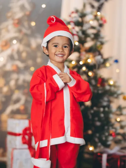 Dressed as Santa Claus in front of a softly lit Christmas tree. This portrait captures the classic holiday spirit, focusing on the child's happy expression and festive attire.