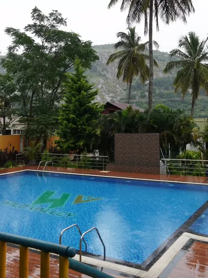 The swimming pool at our Nandi Hills resort, ready for guests to take a dip. The pool area is surrounded by palm trees and offers a view of the hills.