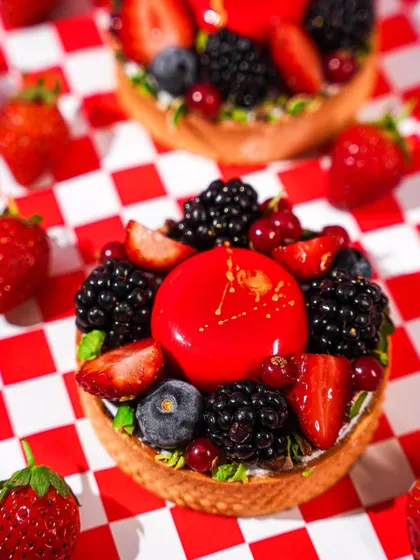 A close-up of a beautiful berry tart on a red and white checkered background. This classic American diner-style setup gives the sophisticated dessert a fun, retro twist.