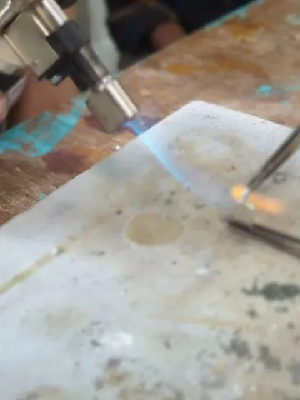 A close-up of a blowtorch heating a small piece of silver, demonstrating the soldering process used to join different parts of a jewelry piece together.