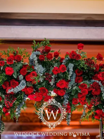A bold and luxurious reception with a red and black color scheme. The decor includes rich red roses, modern crystal candelabras, and a stylish bar with a neon arch backdrop.
