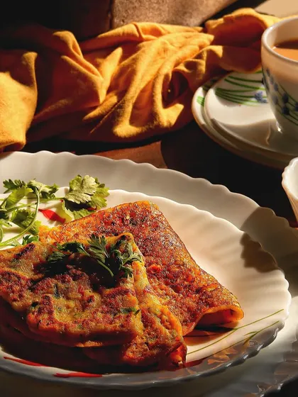A wider shot of the breakfast scene, including the chilla, chutney, and a cup of chai. The beautiful morning light streaming in creates a warm and inviting atmosphere.