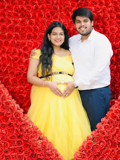 Surrounded by love, literally. This couple looks radiant against a wall of red roses, with her in our sunny yellow gown and him in a coordinated light shirt and dark pants. This setup is perfect for creating a memorable and romantic pregnancy announcement.