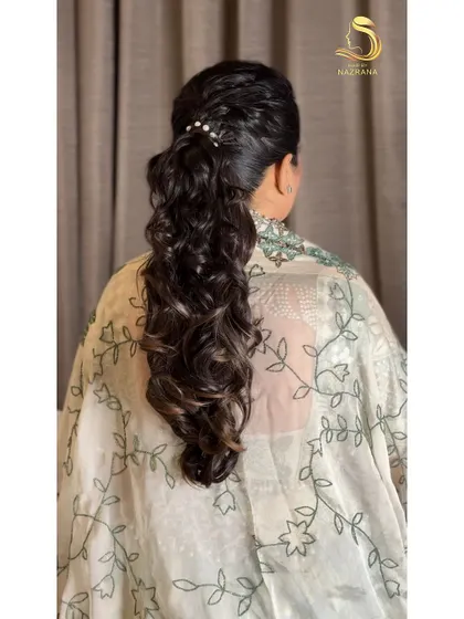 A close-up of the pearl-accented, textured ponytail. The soft curls and gentle volume make this a romantic and timeless choice.