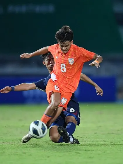 A dramatic, low-angle shot of an Indian U17 player evading a slide tackle. This captures the agility, balance, and quick decision-making that we drill in our training sessions.