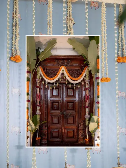 A traditional 'Nishchitartham' or engagement ceremony decor. The soft blue wall with cow motifs provides a unique backdrop for the hanging marigold garlands and brass diyas, blending heritage with a fresh color palette.