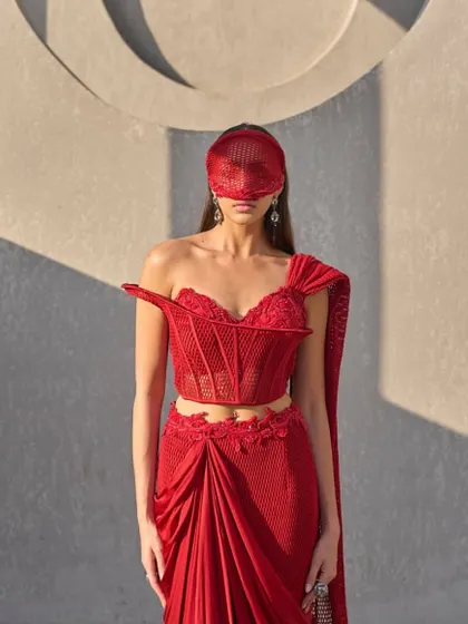 This sari transforms with every movement, fluid and luminous. A sheer mesh corset sculpts the silhouette, while the attached red drape flows like refracted light, embroidered with brilliance.