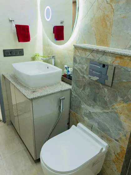A clean and modern bathroom design. This space features a wall-mounted toilet, a sleek vanity, and a backlit oval mirror, all set against a backdrop of beautiful marble-style tiles.