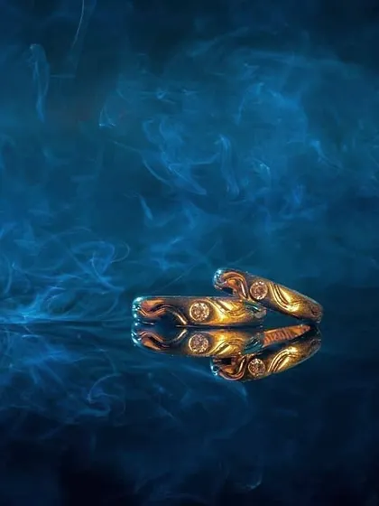 A gold ring is set against a backdrop of swirling blue smoke, creating a mysterious and luxurious feel. This product shot uses atmosphere to enhance the appeal of the jewelry.