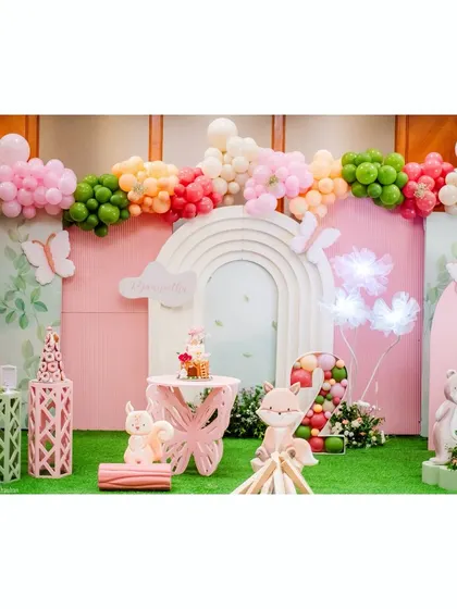 A wide view of our magical woodland party. The setup includes a colorful balloon garland, a large arched backdrop, and cute animal props like a fox and a bear, all set on a lush green lawn.