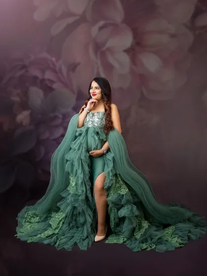 A soft, painterly portrait. The floral background in muted tones complements the intricate green gown, creating a romantic and artistic image.