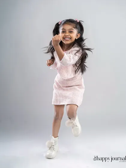 A girl in a stylish pink outfit jumps for joy in the studio. Her energy is infectious in this fun and dynamic shot.