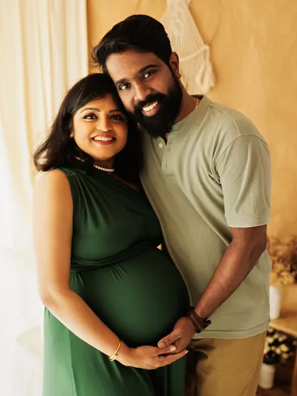 A classic and happy portrait of an expecting couple in a warm, natural light setting. Their direct gaze and smiles invite you into their joyful moment.