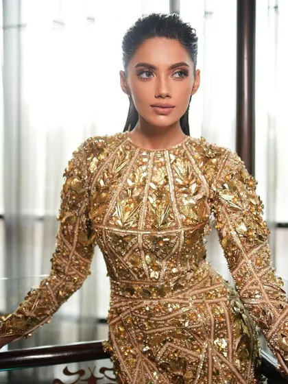A close-up of a glamorous look in a gold-leafed dress. The makeup is kept clean and sharp to complement the intricate outfit, focusing on a flawless complexion and a defined eye.