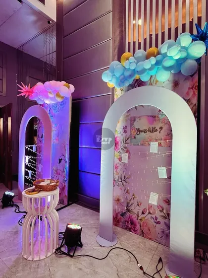 This modern and chic entrance features two illuminated arches with a floral backdrop. One arch includes a fun activity where guests can hang personal notes for the parents-to-be, creating an interactive and welcoming experience from the moment they arrive.