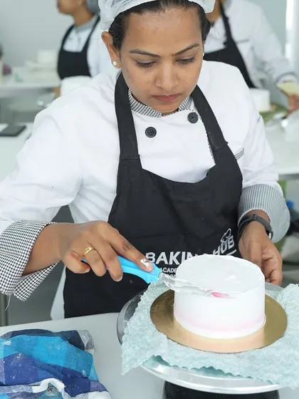 Using a scraper to achieve perfectly smooth sides on a cake. We provide all the professional tools and teach you how to use them effectively to get bakery-quality results.