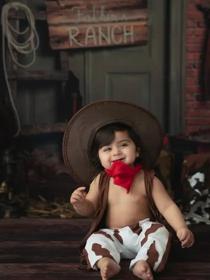 Howdy, partner! This little cowboy is ready for adventure in our rustic ranch-themed setup. The oversized hat and cow-print pants add to the adorable charm.