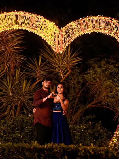 A beautiful night shot of a couple making a heart sign within a large, illuminated heart structure.