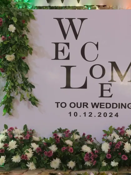 A classic and elegant welcome sign for a wedding. The simple typography, framed by fresh greenery and flowers, provides a sophisticated first impression for arriving guests.