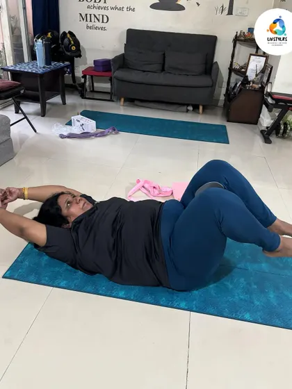 A client performs a core-strengthening exercise using a ball between her knees. This engages the inner thighs and deep abdominal muscles, enhancing core stability.