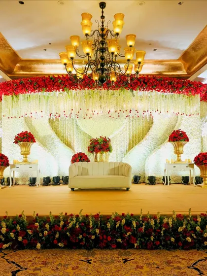 A closer view of the magnificent red and white reception stage, showcasing the dense floral work and the heart-shaped draping of flower strings.