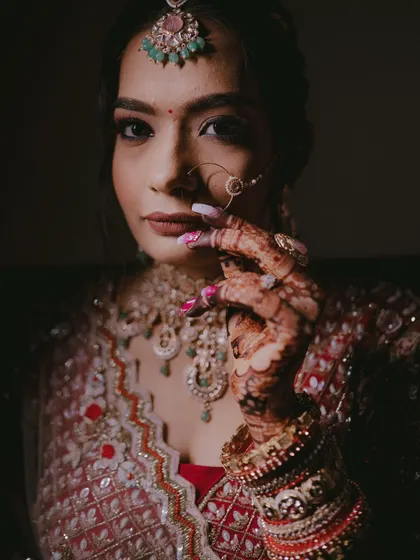 A powerful portrait of the bride looking directly at the camera, her hand gently touching her face, showcasing her bold makeup and jewelry.