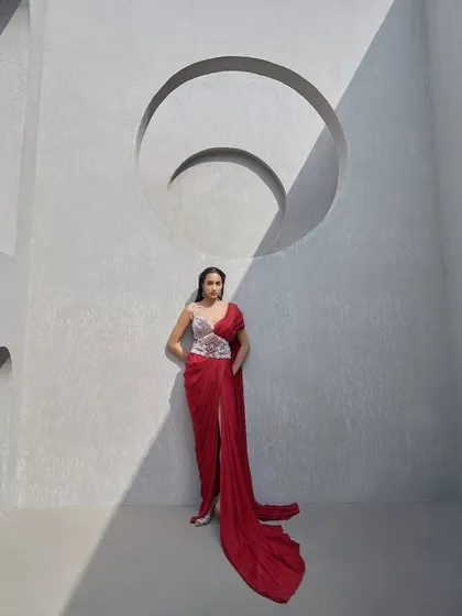 This look reimagines the sari with a deep crimson drape sculpted by a hand-embellished pearl corset belt. It is a fusion of Indian elegance and contemporary couture for the woman who bends tradition to her will.