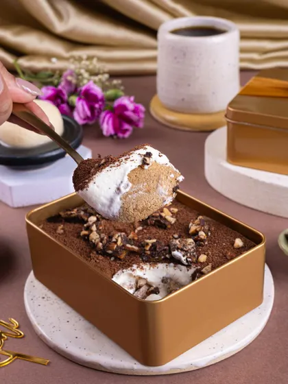 A dynamic action shot of the Rasgulla Tiramisu, capturing the moment a spoon digs in to reveal the creamy layers inside.