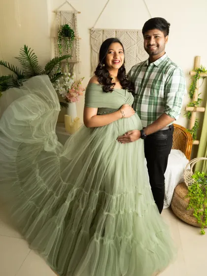 A happy, smiling portrait of an expecting couple. The flowing green gown and casual shirt make for a relaxed yet beautiful look.