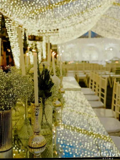 A long dining table set for the sangeet feast, with candles and flowers reflected in the mirrored surface. The repetition of lights creates a stunning visual corridor.