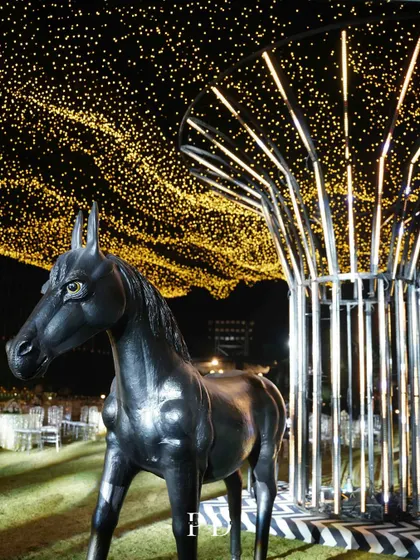 A unique and artistic decor element for a Sangeet, featuring a black horse statue under a modern light installation and a canopy of fairy lights.